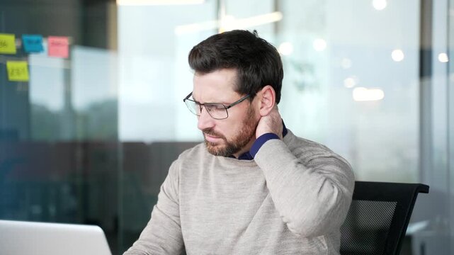 Close up of businessman suffering from neck pain working on laptop in office. Mature professional massages sore neck muscles, feeling stiffness, tension, discomfort caused by prolonged computer work.