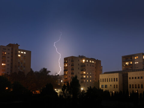 Powerful lightning strike illuminates the night sky above residential apartment buildings