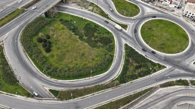 Aerial view of winding roads interweaving with circular roundabouts, creating a mesmerizing pattern of grey asphalt and green vegetation, Thessaloniki, Thessaloniki, Greece.