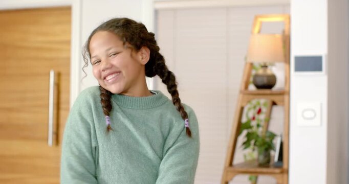 Girl aged eight swinging pigtails, smiling and spreading arms at entryway by ladder shelf