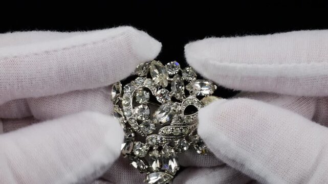 The focus is on a vintage silver-tone metal brooch adorned with clear shimmering crystals. This elegant accessory features a complex design with prong-set rhinestones that capture.