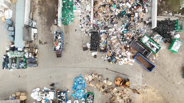 Aerial view of waste sorting and recycling process showing piles of garbage, containers, and vehicles in a waste management facility, highlighting the organization of recyclable materials