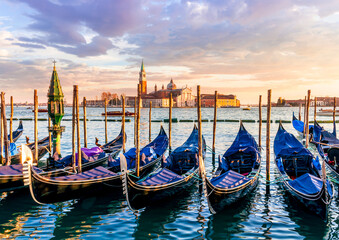 row of parked venetian gondola boats in Grand canal of Venice. Beautiful sunset or sunrise landscape with gondolas in blue water of Venice. © Yaroslav