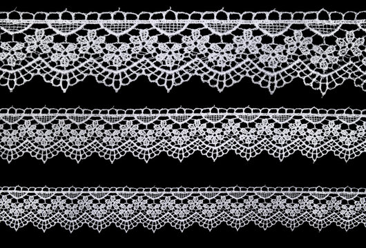 Set of white lace ribbons on black background with delicate openwork pattern. Vintage lace trims for design and decoration.