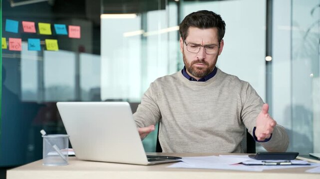 Unhappy businessman reviewing financial documents and looking at laptop screen sitting at desk in office. Mature entrepreneur analyzing results, disappointed and concerned about business performance.
