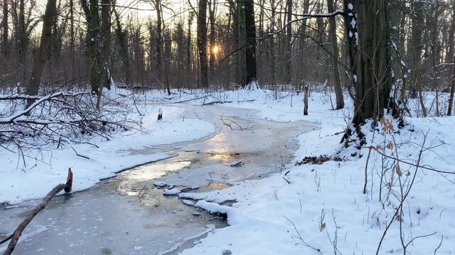 Snow covered forest and little frozen river in winter sunset view