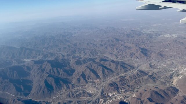 High quality 4K 60fps aerial view from airplane window flying over Al Faya desert mountains during descent to Sharjah Dubai airport UAE at sunset with golden light and hazy horizon landscape