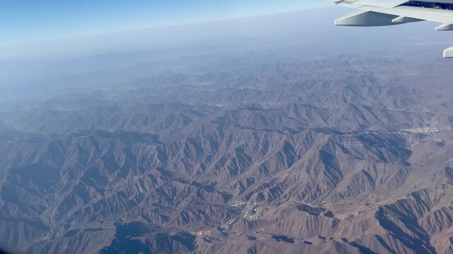 High quality 4K 60fps aerial view from airplane window flying over Al Faya desert mountains during descent to Sharjah Dubai airport UAE at sunset with golden light and hazy horizon landscape