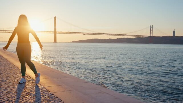 Graceful woman dancing at sunset on lisbon's riverfront promenade