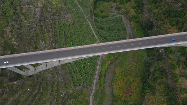 Aerial top down view of cars driving on the Los Tilos bridge. The massive concrete structure crosses a deep green canyon in La Palma