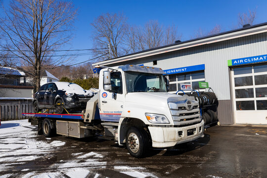 Quebec City, Quebec, Canada, March 21, 2026 - A Canadian Automobile Association (CAA)&nbsp;Quebec club tow truck with Fiat 500 car on its flatbed in front of garage 