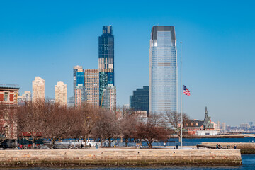 Obraz premium Jersey City waterfront skyline with American flag and winter trees on a clear blue day