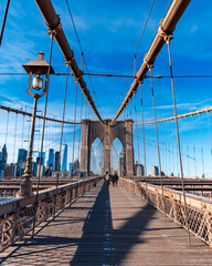 Fototapeta premium Front-facing view along the pedestrian walkway of the Brooklyn Bridge with suspension cables, historic lampposts and the stone towers under a clear blue sky in New York City, USA. 