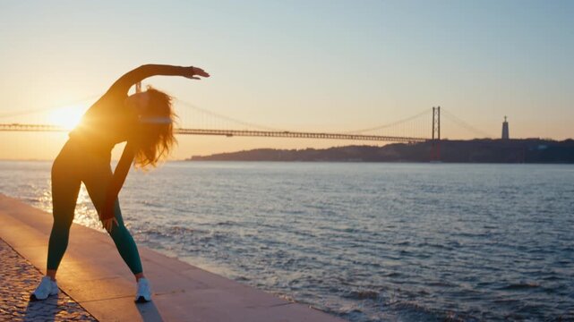 Woman stretching her body during sunset by the river in lisbon