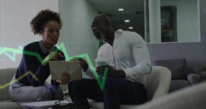 Woman holding tablet to man, tapping, pointing and reviewing finance charts with green or yellow lin