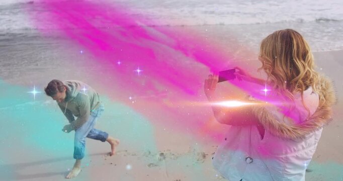 Woman filming man, sending pink-teal mist from phone at him, causing stumble then smile for content