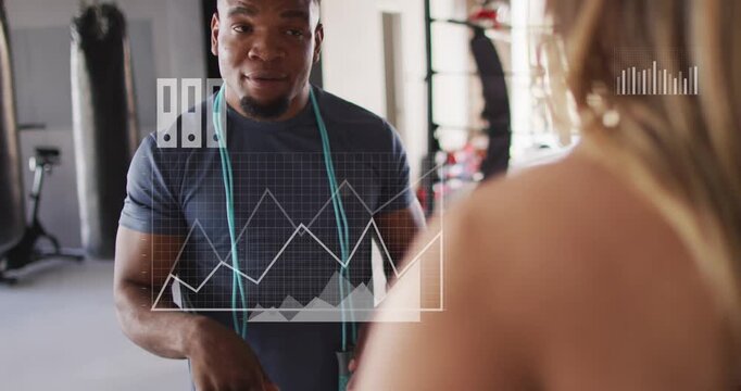 Vertical video: Pointing trainer in dark tee coaching client in gym, with teal jump rope and charts