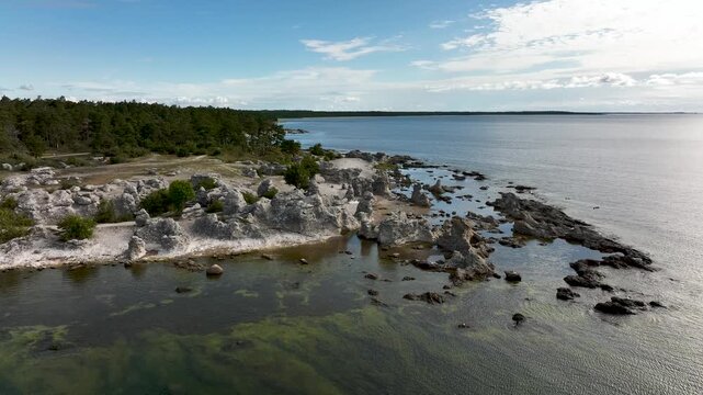 Drone flying along limestone sea stacks and rocky coastline at Folhammar raukf&auml;lt, Gotland, Sweden with Baltic Sea shoreline and coastal forest