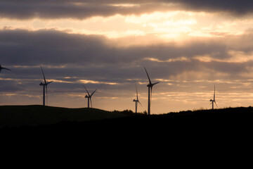 Obraz premium Wind energy turbines silhouetted against a dramatic sunset sky