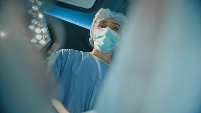 Low angle shot of female surgeon standing near operating table, performing surgical procedure and using sterile medical instruments