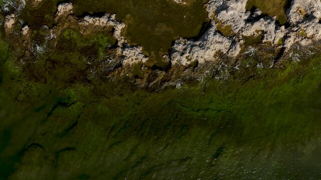 Top down drone view of waves moving over rocky coastline revealing underwater patterns and limestone formations in the Baltic Sea at Gotland, Sweden
