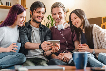Obraz premium Cheerful interracial friends sitting on sofa with mobile phone at home, watching content, chatting online, social networking, modern lifestyle, entertainment and communication concept