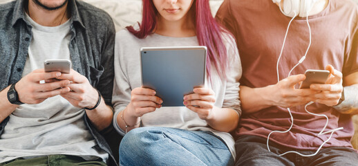Gadgets addiction. Cropped of young people using smartphones and tablet on couch at home, browsing social media, chatting online, digital lifestyle, mobile technology, communication leisure concept