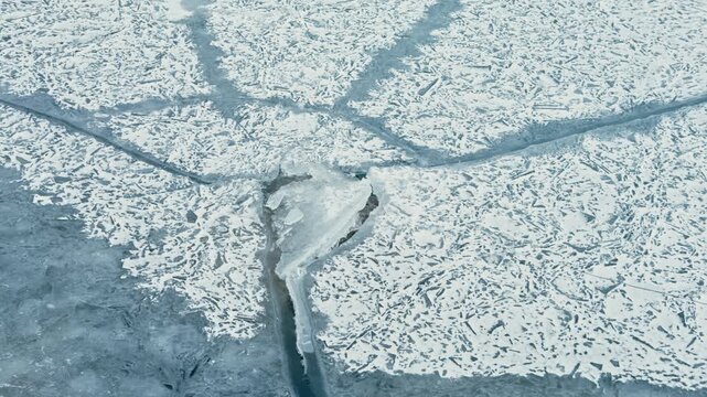 Frozen lake shows a pattern of cracks across the icy surface, with layers of snow and frost visible. The scene captures the harshness of winter in a remote setting.