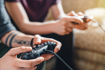 Close up of male friends using joysticks to play video games at home, sitting on couch, gaming console, entertainment, fun, leisure, digital lifestyle, social interaction, modern technology concept © InsideCreativeHouse