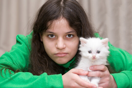 A teenage girl plays with a white kitten