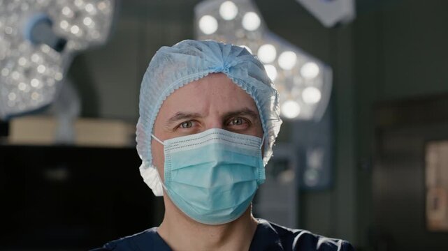 Caucasian surgeon wearing sterile mask, standing in operating room and looking at camera