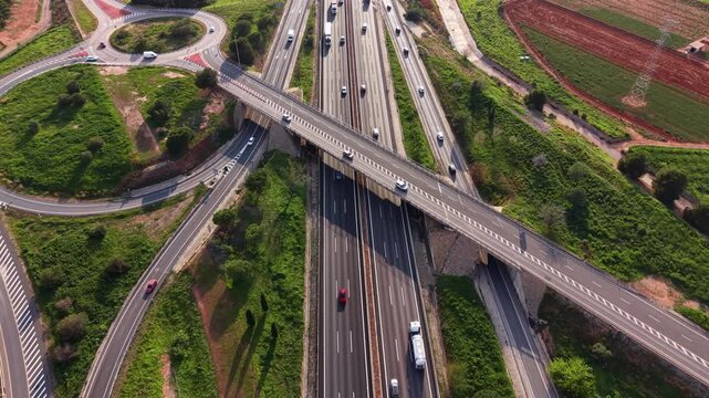 Aerial view of multilane highway interchange with overpass and roundabout, showing flowing traffic across ramps and bridges through green rural surroundings