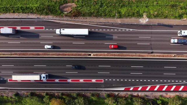 Top-down aerial of multilane highway with dashed lane lines, solid shoulders and red white chevron hatch markings guiding merges while cars and trucks move at speed
