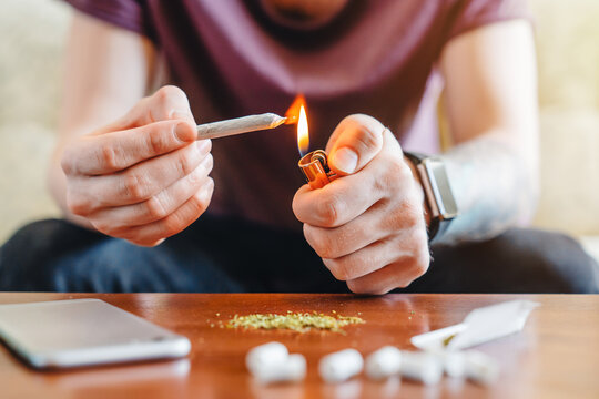 Close up of man holding cigarette and lighter at home, lighting cigarette, addiction, indoor lifestyle, personal habit, relaxation, smoking concept, focus on hands, domestic environment and leisure