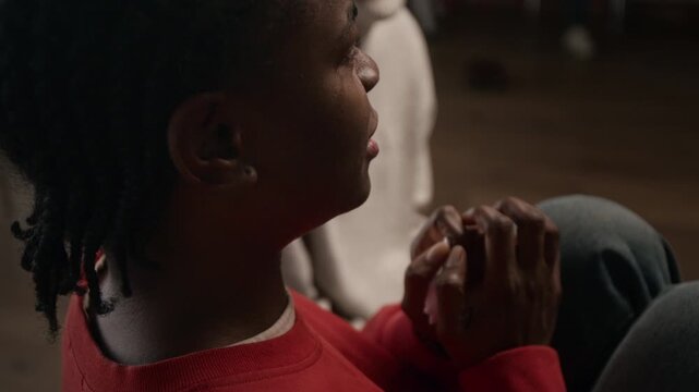 Cinematic close up shot of young Black woman crying while sitting on chair during support group meeting and sharing emotional life story wiping tears with tissue