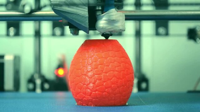 A video showcasing a 3D printer creating an orange object in a factory