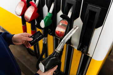 Hand holding bank card near gasoline nozzle during refueling. © Rabizo Anatolii
