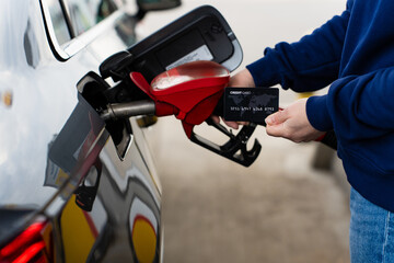 Driver holding credit card beside fuel pump during refueling. © Rabizo Anatolii