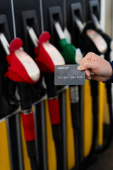 Hand holding credit card at gas station highlighting rising fuel costs.