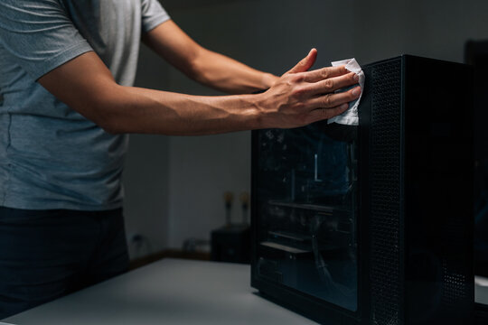 Cropped shot of technician cleaning dust from computer case in dark workshop, emphasizing importance of regular maintenance for optimal performance and hygiene.