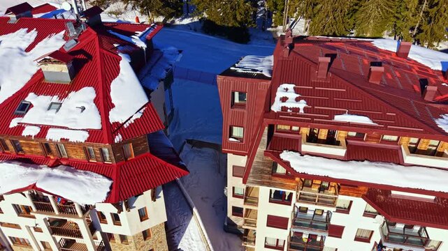 Snow rests on the roofs of buildings in a ski resort area. The scene shows the outline of the structures and the layout of the surrounding terrain.