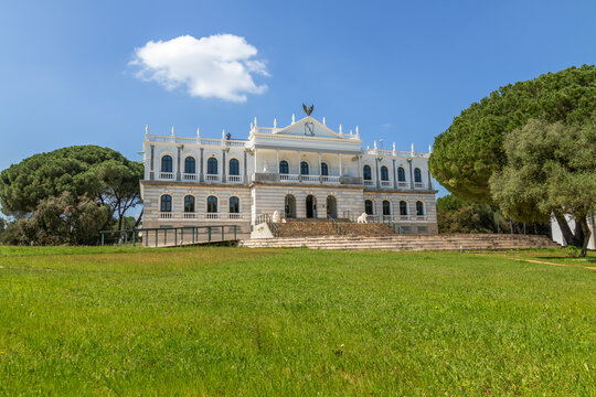 Neoclassical facade of Acebron Palace in Donana National Park, Almonte, Spain. Historic white building surrounded by pine forest under a blue sky.