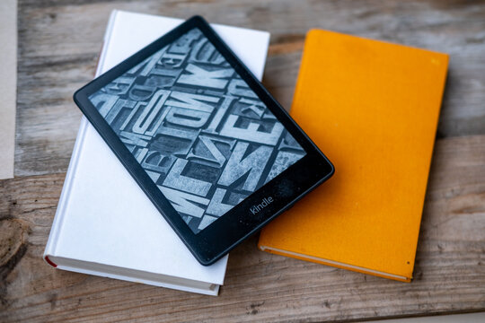 modern Kindle e reader on stack paper books, black e-book reader, digital book Kindle, tablet computer device displaying text electronically, electronic paper technology, reading fiction, text editing