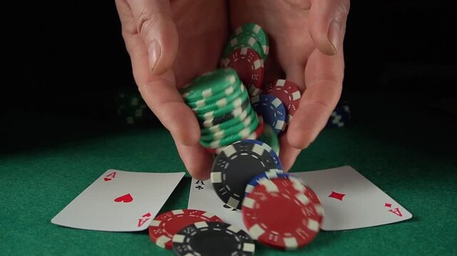 Hands releasing colorful poker chips over playing cards on a green felt table, showcasing a dynamic moment in a card game setting