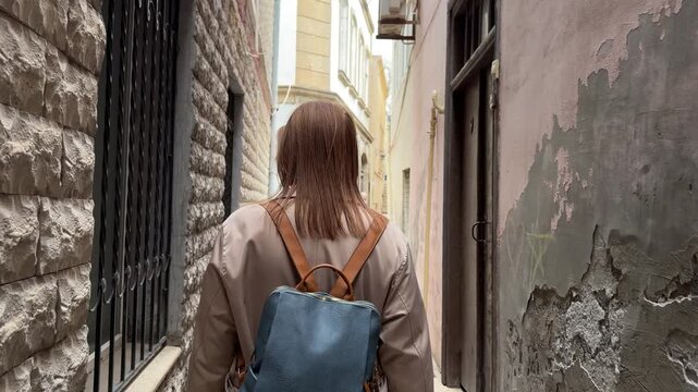 Back view of a female traveler walking through a narrow street in the old city of Baku, Azerbaijan, surrounded by aged stone walls and historic architecture, suitable for travel