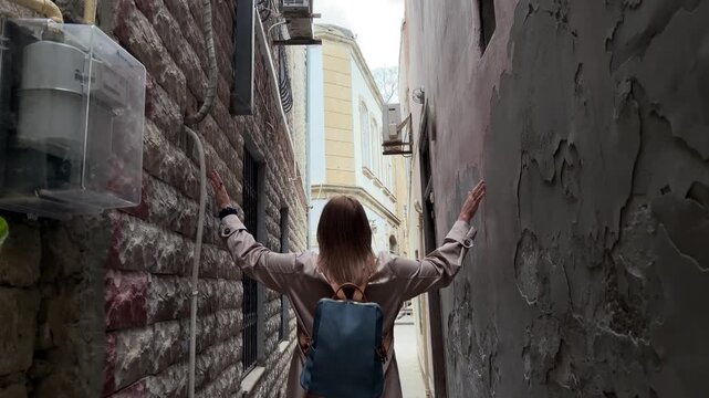 Back view of a female traveler walking through a narrow street in the old city of Baku, Azerbaijan, surrounded by aged stone walls and historic architecture, suitable for travel