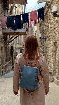 Rear view of woman with backpack walking through a narrow alley with laundry lines for travel, exploration, and city life.