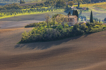 Naklejka premium Tuscan farmhouse surrounded by plowed fields and olive groves, Italy.