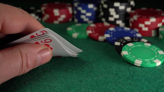 Hand reveals playing cards in a poker game, showcasing a sequence of card values and colorful poker chips on a green felt table