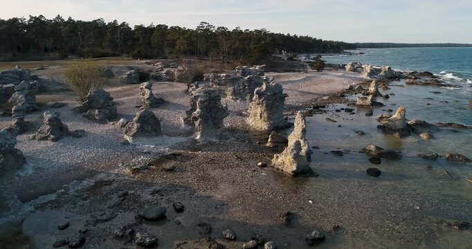 Left to right pan revealing waves hitting limestone coast framed between rauks at Folhammar, Gotland, Sweden